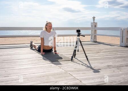 Junge sportliche Frau beim Training und Videoaufnahme am Strand Stockfoto