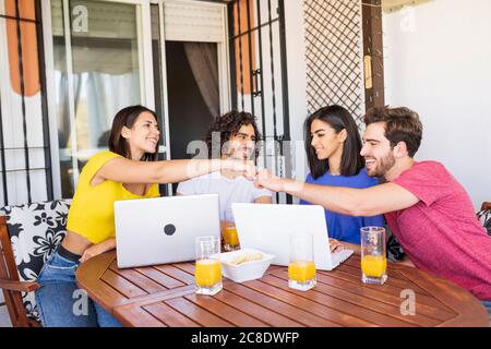 Lächelnder Mann und Frau geben Faust Beule, während sie mit sitzen Freunde im Hinterhof Stockfoto