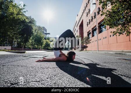 Junge Frau, die an sonnigen Tagen Yoga auf der Straße der Stadt durchführt Stockfoto