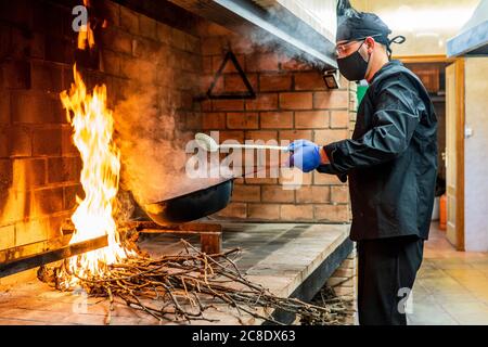 Traditionelle Küche von Paella in der Restaurantküche, Koch trägt Schutzmaske Stockfoto