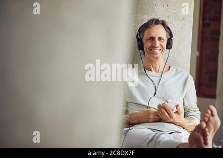 Porträt eines lächelnden älteren Mannes mit Kopfhörern, die Musik hören Eine Loft-Wohnung Stockfoto