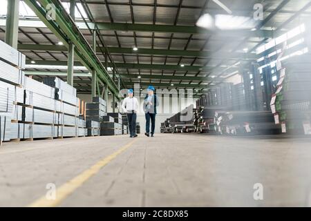 Zwei Geschäftsleute, die sich treffen und in einer Fabrik spazieren gehen Stockfoto