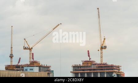 Gelbe Turmkräne und unfertige Gebäudekonstruktion gegen dramatische bewölkt grauen Himmel. Bauprozess, Stadt, Engineering, Stadt entwickeln Stockfoto