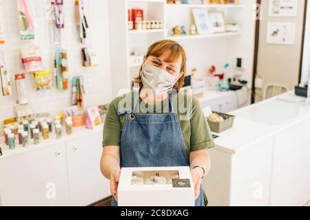 Weibliche Bäcker tragen Maske liefern Cupcake-Box, während im Stehen Speichern Stockfoto