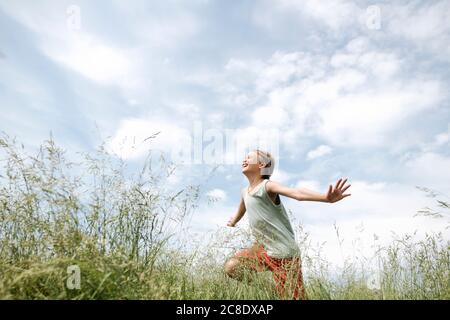 Porträt eines glücklichen Jungen, der mit Armen auf einem Feld läuft Ausgestreckt Stockfoto