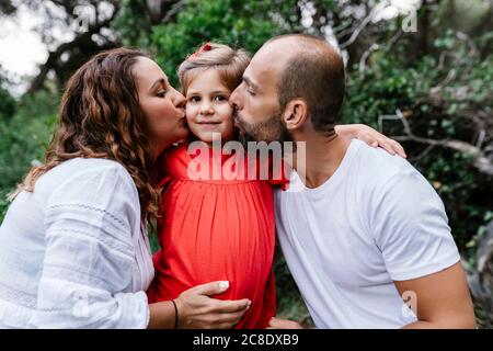 Eltern küssen Mädchen auf Wangen im Wald Stockfoto