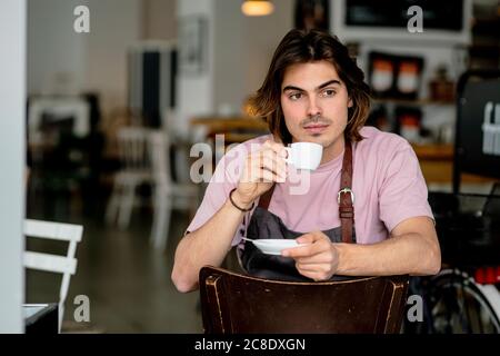 Nachdenklicher männlicher Besitzer, der Kaffee trinkt, während er auf einem Stuhl sitzt Café Stockfoto