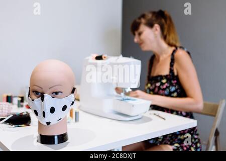 Nahaufnahme der Schaufensterpuppe mit Maske auf dem Tisch, während weibliche Schneiderin Arbeiten im Hintergrund Stockfoto