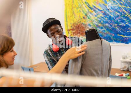 Lächelnder junger Mann, der Modedesigner ansieht, der Schaufensterpuppe hält Designstudio Stockfoto