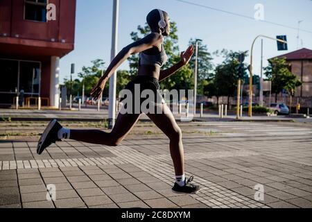 Sportlerin, die Musik über Kopfhörer hört, während sie auf der Straße läuft In der Stadt Stockfoto