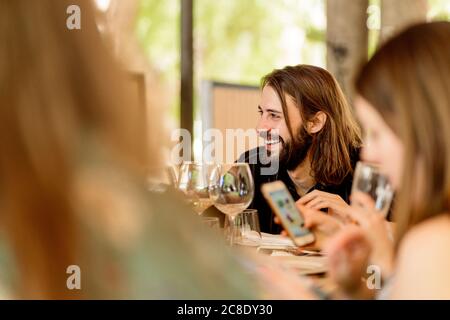 Lächelnder junger bärtiger Mann, der mit Freundinnen im Restaurant sitzt Stockfoto