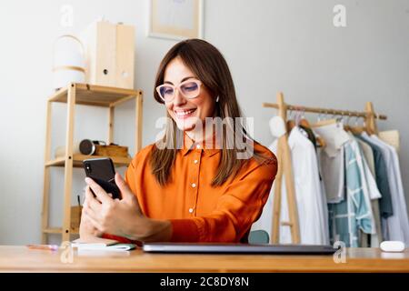 Weibliche Modedesignerin, die zu Hause am Schreibtisch sitzt Smartphone Stockfoto