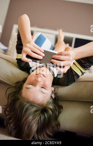 Junge spielt Spiele auf dem Smartphone, während er auf dem Sofa sitzt Zu Hause Stockfoto