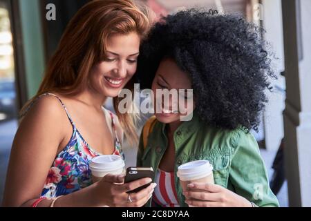 Freundinnen mit Kaffee, um mit dem Smartphone zu gehen Stockfoto