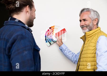 Männlicher Architekt, der im Stehen dem Bauarbeiter Farbmuster zeigt Durch die Wand im Haus Stockfoto
