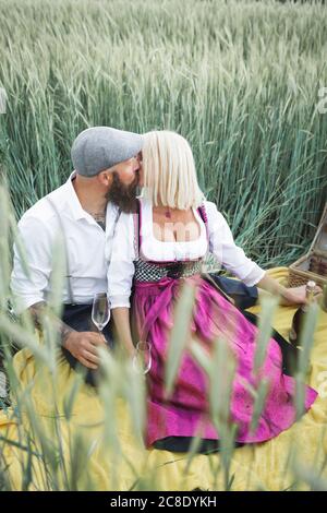 Reifes Paar hält Champagner Gläser küssen während sitzen inmitten Pflanzen An Land Stockfoto