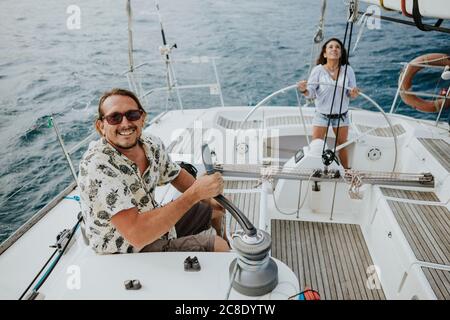 Mann, der mit Winde manövriert, während Frau Segelboot im Meer fährt Stockfoto