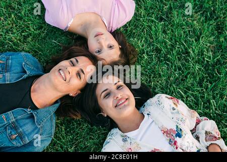 Lächelnde Mutter mit den Töchtern, die auf dem grasbewachsenen Land im Park liegen Stockfoto