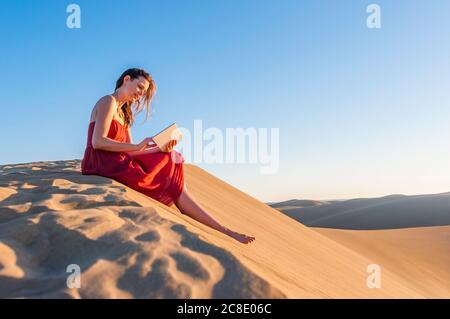 Frau in rotem Kleid sitzt in den Dünen mit Tablet, Gran Canaria, Spanien Stockfoto