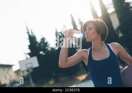 Teenager-Mädchen, das Wasser aus der Flasche trinkt, während sie Basketball hält Stockfoto