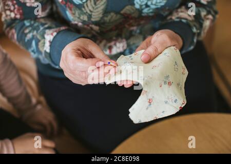 Reife Frau hält gerade Stift und florale Textil zum Nähen Gesichtsmaske zu Hause Stockfoto