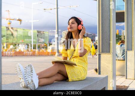 Junge Frau, die Musik hört, während sie auf einer Betonbank sitzt Stadt Stockfoto