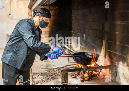 Traditionelle Küche von Paella in der Restaurantküche, Koch trägt Schutzmaske Stockfoto