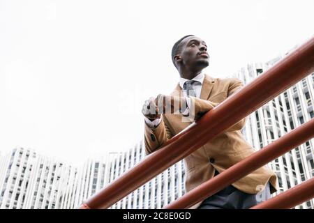 Junger Geschäftsmann, der sich auf ein Geländer in der Stadt stützt Weg Stockfoto