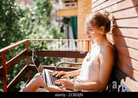 Junge Frau, die auf dem Balkon am Laptop arbeitet Stockfoto