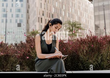 Weibliche professionelle Schreiben in Notizblock während sitzen gegen Pflanzen Stockfoto