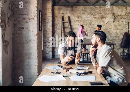 Kreatives Team, das am Tisch im Loft-Büro sitzt Stockfoto