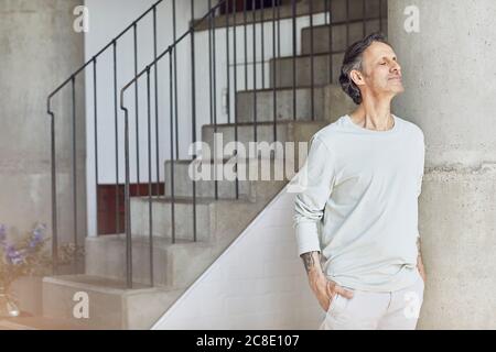 Älterer Mann mit geschlossenen Augen, der sich gegen eine Säule lehnt Eine Loft-Wohnung Stockfoto