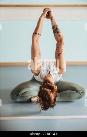 Ballerina streckt die Arme, während sie sich im Tanz auf dem Boden beugt studio Stockfoto