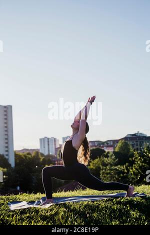 Junge Frau praktiziert Yoga in Kriegerposition im Stadtpark Gegen klaren Himmel Stockfoto