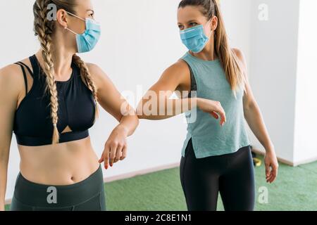 Zwei sportliche Frauen tragen Gesichtsmasken geben Ellenbogen Beule an Fitnesscenter Stockfoto