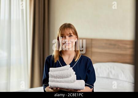 Lächelndes Zimmermädchen hielt Handtücher, während sie im Hotelzimmer stand Stockfoto