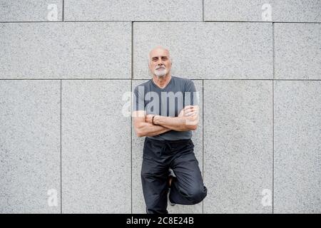 Selbstbewusster älterer Mann mit gekreuzten Armen, der gegen die Wand steht Stadt Stockfoto