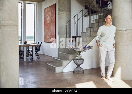 Älterer Mann, der sich in einer Loft-Wohnung an einer Säule lehnt Stockfoto