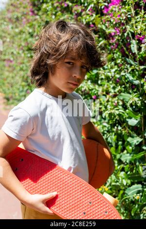 Nahaufnahme eines Jungen mit Basketball und Skateboard neben Pflanzen stehen Im Park Stockfoto