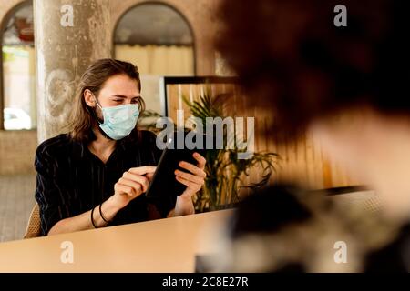 Junger Mann trägt Maske während des Sitzens und mit digitalen Tablet Im Restaurant Stockfoto