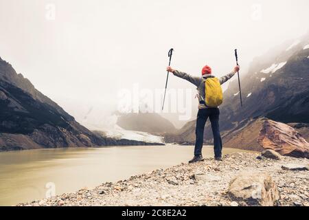 Mann mit ausgestreckten Armen und Wanderstöcken am See in Patagonien, Argentinien Stockfoto