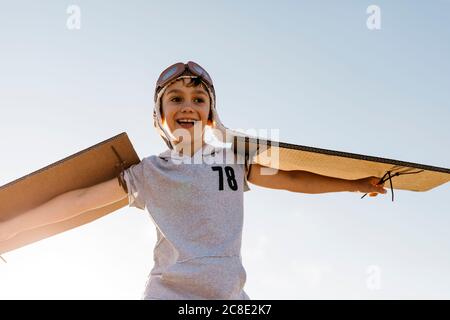 Junge mit Fliegermütze und Pappflügeln gegen den Himmel Stockfoto