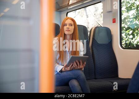 Nachdenkliche junge Frau hält digitales Tablet, während sie im Zug sitzt Stockfoto