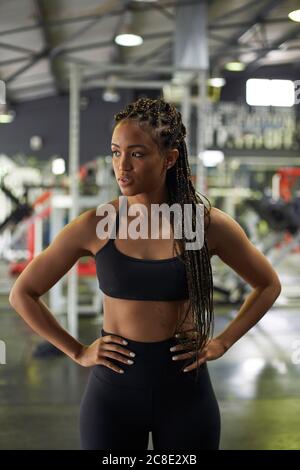 Selbstbewusste weibliche Athletin mit Armen Akimbo im Fitnessstudio stehen Stockfoto