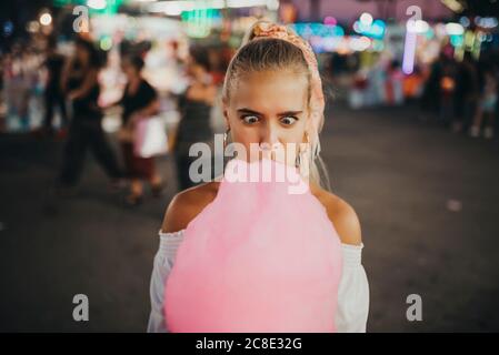 Nahaufnahme einer Frau, die Gesicht macht, während sie Zuckerwatte isst Vergnügungspark Stockfoto