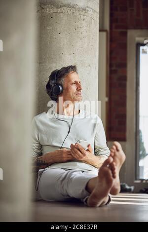 Älterer Mann mit Kopfhörern, der Musik in einer Loft-Wohnung hört Stockfoto