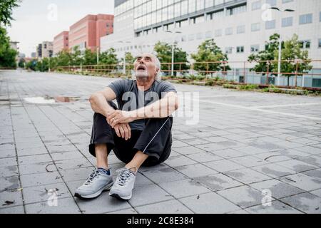 Müder älterer Mann mit offenem Mund und aufblickender Sitzungsperhoheit Auf Fußweg in der Stadt Stockfoto