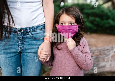 Tochter trägt Schutzmaske und hält die Hand ihrer Mutter Stockfoto