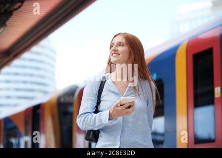 Junge Frau mit Smartphone am Bahnhof Stockfoto