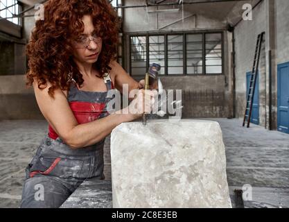 Weiblicher Steinmetz mit Lockenhaar Schnitzstein im Studio Stockfoto